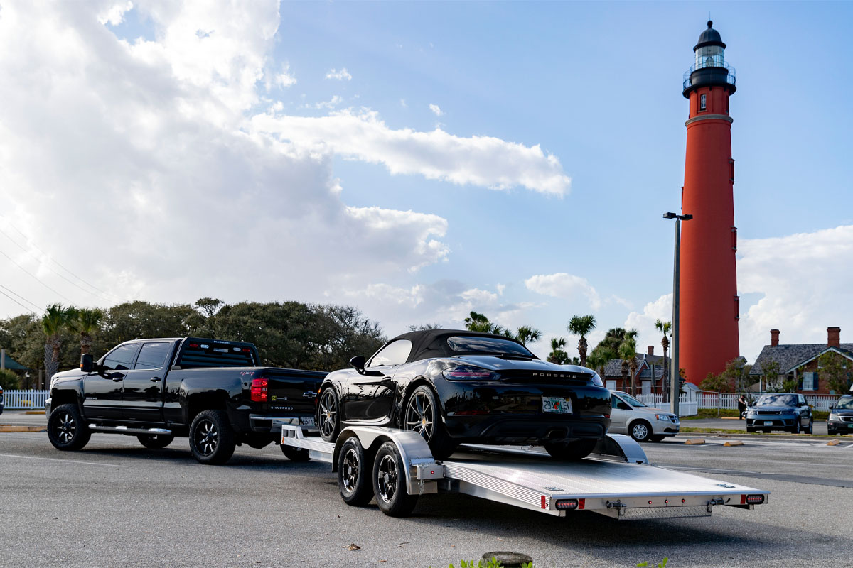 Back View Of Black Truck Hauling Black Car On Polaris Open Car Hauler